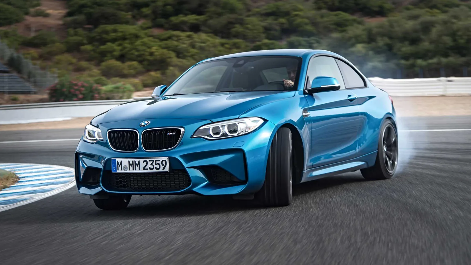 Long Beach Blue 2016 BMW M2 Coupe drifting on a race track with tire smoke