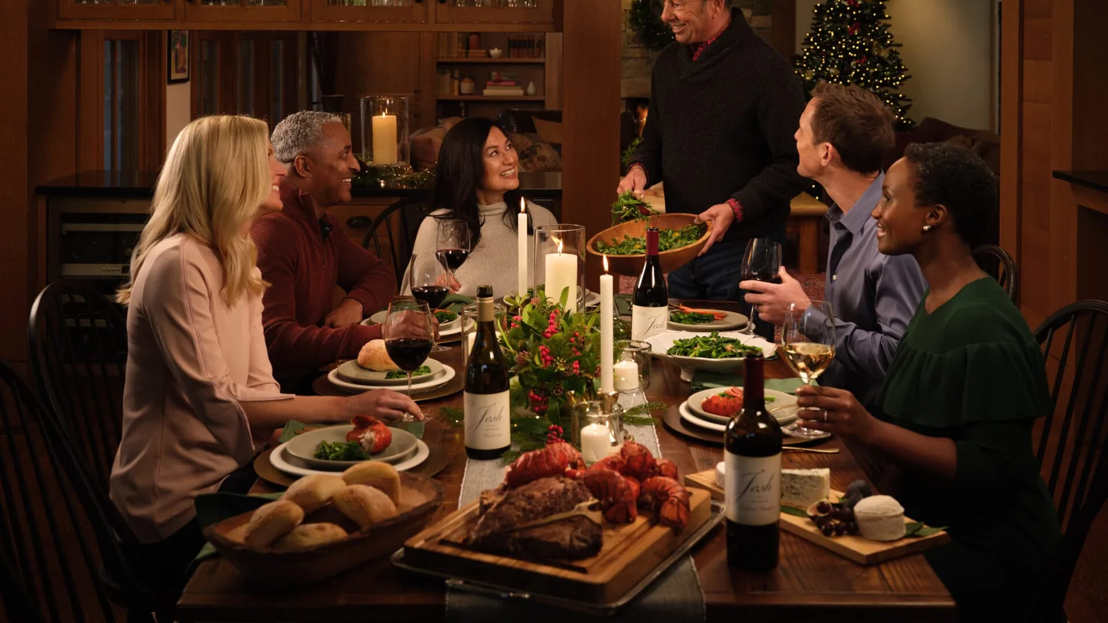 Josh Cellars founder Joseph Carr serving dinner to friends around a candlelit table with bottles of Josh Cellars wine